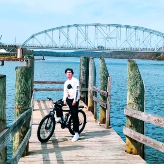 Un hombre parado en un muelle con su bicicleta, disfrutando de la vista del agua.