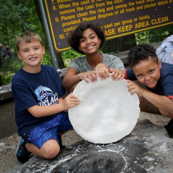 three children showing their plastic dinosaur track