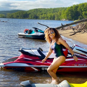 Woman in bathing suit standing next to jet skis on sandy beach.