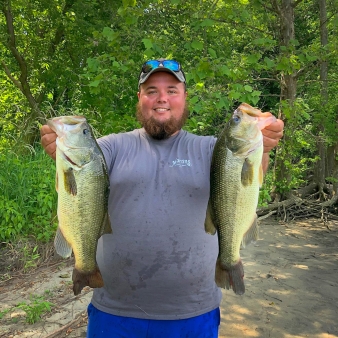 A man proudly holds two large bass he caught while fishing.