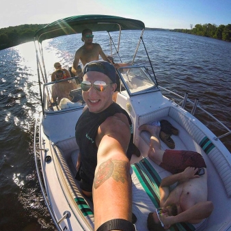 Un hombre sonriendo mientras se toma una selfie en un barco, capturando un momento de alegría en el agua.