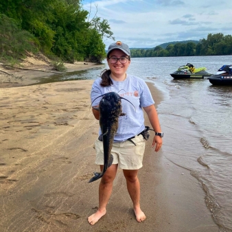 A person on a sandy beach happily holds a fish they caught.