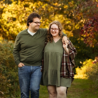 Pareja comprometida sonriente rodeada de follaje de otoño.