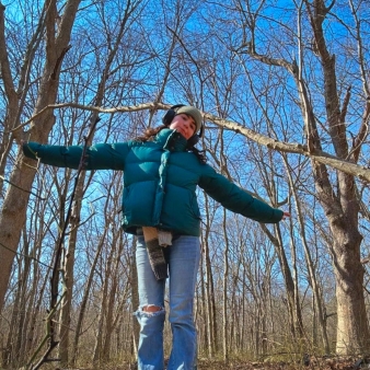 Excursionista femenina con chaqueta verde parada entre árboles en el bosque.