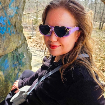 Señora con elegantes gafas de sol de color púrpura sentada sobre una superficie rocosa.