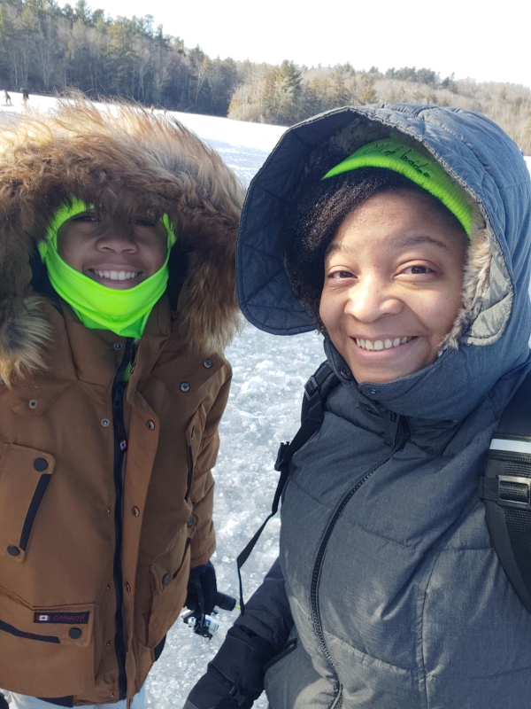 Dos personas abrigadas con abrigos de invierno con capucha sonríen en esta selfie tomada sobre la superficie helada del estanque Burr.