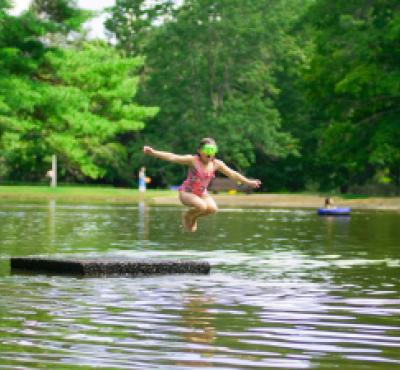 Chica saltando desde el muelle en el estanque Mashamoquet