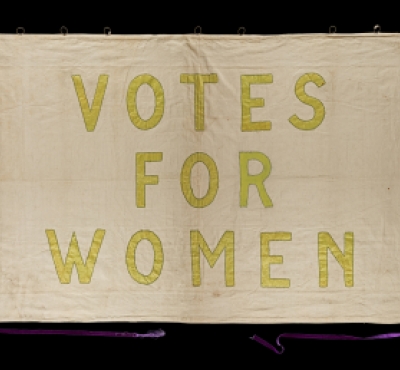 Banner with yellow text reading "Votes for Women"