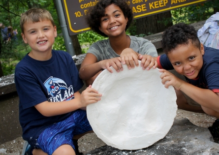 tres niños mostrando su huella de dinosaurio de plástico