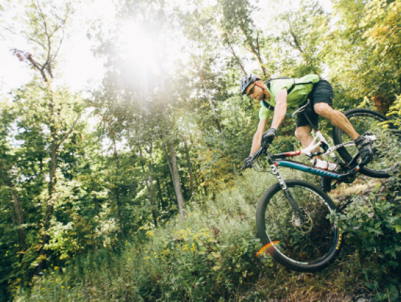 Hombre ciclismo de montaña a través de bosques