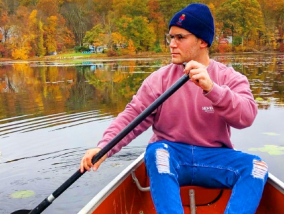 Un hombre con un suéter rosa rema en una canoa a través de un estanque tranquilo.